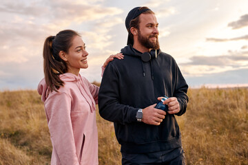 Outdoor portrait of positive couple in nature countryside relaxing before or after jogging. attractive female and male in hoodie laughing, talking. wellbeing, healthy lifestyle, human emotions