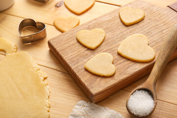 Board with raw heart shaped cookies on wooden table, closeup. Valentines Day celebration