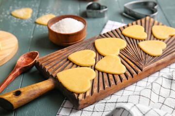 Board with raw heart shaped cookies on dark wooden background, closeup. Valentines Day celebration