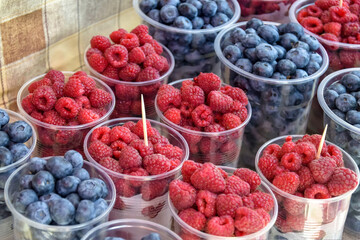Fresh delicious berries blueberries and raspberries in plastic cups. Colorful sweet berries close-up. Market trading. Selective focus.