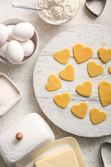Wooden board with raw heart shaped cookies and ingredients on light background. Valentines Day celebration