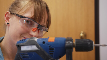 closeuo view of a woman with safety glasses using a drill into a wall, repair concept. High quality...