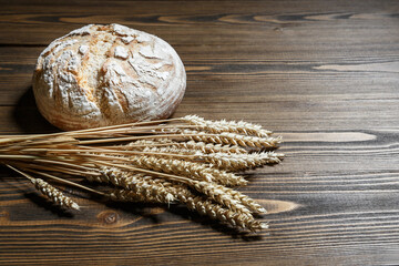 Fresh baked bread loaf and wheat ears lying on a wooden background.