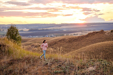 Woman Training, jogging. Free young woman runs in summer field at sunset. healthy beautiful fit caucasian lady is engaged in fitness, jogging in country in sun. Jogger breathes fresh air on field.