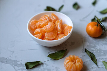 Fresh mandarin orange fruits or tangerines with leaves on a gray background or table in a white plate