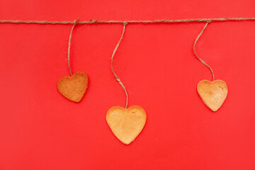 Sweet heart shaped cookies hanging on rope against red background. Valentines Day celebration