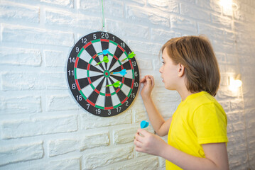 boy standing in front of a target for playing darts, counting points after the game