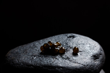 Few eggs of caviar lying on rough black stone.