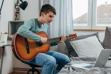 Teenage boy learns how to play a guitar online