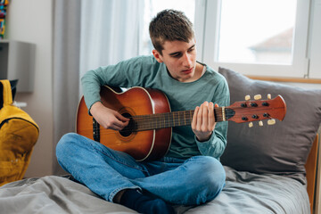 A teenage boy concentrates on learning how to play guitar