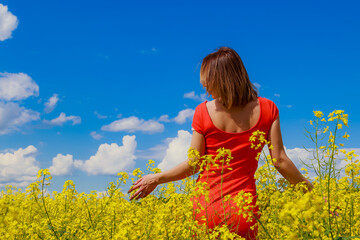 Young pretty woman in a colored dress on Lightning cheerful yellow background blooming rapeseed fields.