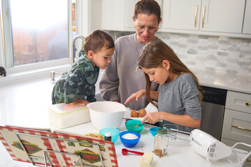 A mother is baking in the kitchen with her young son and daughter