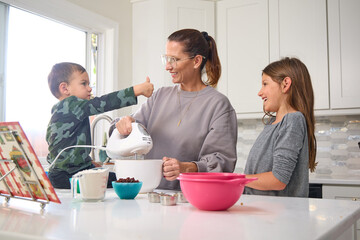 A mother is baking in the kitchen with her young son and daughter