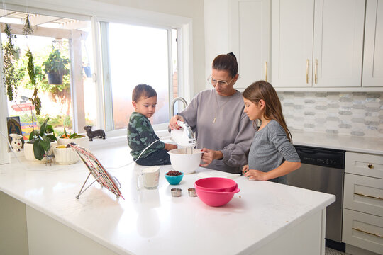A mother is baking in the kitchen with her young son and daughter