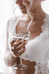 Bride holding a glass of champagne in her hand. The bride is drinking champagne in a hotel room.
