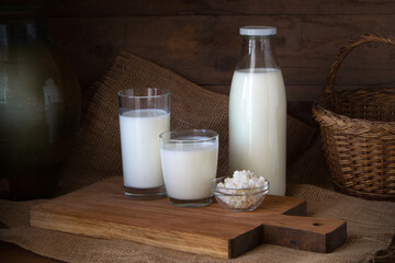 A bottle of milk, a glass of yogurt and kefir and some cottage cheese on a wooden background.