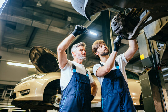 Two handsome professional car mechanic are Investigating Rust Under a Vehicle on a lift in service using a LED lamp