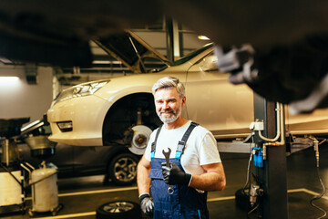 Pleased proffesional grey haired american car technician in the workplace.