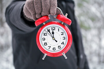 the hand holds a red alarm clock showing 12 o'clock, noon or midnight.