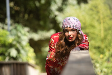 Beautiful young woman in a typical Moroccan red suit, embroidered with gold and silver threads, with a scarf with coins on her head, leaning on a wooden railing. Concept ethnicity, Marrakech, Arab.