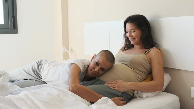 Lesbian woman listening the belly of her lesbian pregnant couple in bed