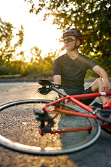 young Biker man resting during riding the bike in nature countryside, sit on road. Handsome caucasian young Male athlete in cycling gear practising outside. Travel and extreme sport concept.