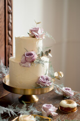 Elegant white wedding cake with violet roses on a golden plate on a wedding reception 