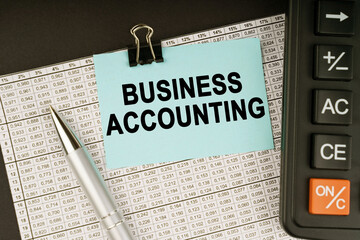 On financial reports lies a calculator, a pen and a sticker with the inscription - BUSINESS ACCOUNTING