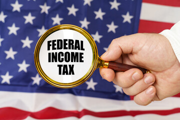 In front of the American flag, a man holds a magnifying glass in his hand with the inscription - federal income tax - obrazy, fototapety, plakaty