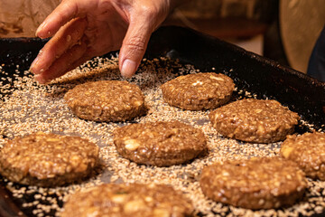 Close-up de mão feminina colocando na assadeira cookies de banana com castanha de caju sendo preparados para o cozimento. 