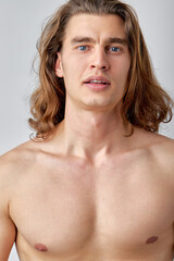 Portrait of attractive shirtless guy posing isolated over light grey color background. Long haired caucasian man with athletic torso looking at camera. Isolated on background. copy space