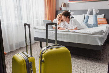 selective focus of suitcases near young travelers watching movie on laptop in modern hotel bedroom.