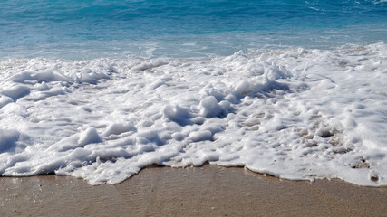 wet sand, white sea foam and blue sea close up