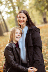 Vertical merry, cheerful laughing family of mother and little daughter embracing, looking at camera, hugging tohether