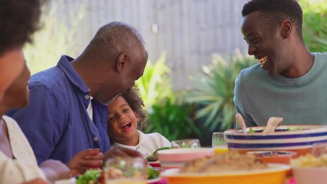 Multi-generation family sitting around table at home eating and enjoying meal together - shot in slow motion