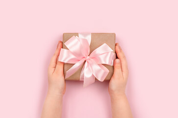 Girl's hands holding gift box with pink ribbon on pastel pink background