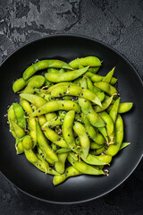 Boiled Edamame Soy Beans with sea salt in a plate. Black background. Top view