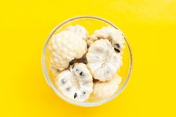 Custard apple in glass bowl on yellow background.