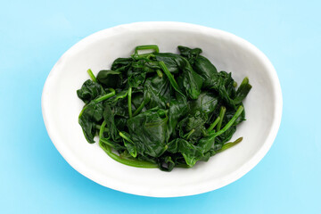 Boiled spinach in white bowl on blue background.