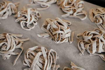 Homemade pasta. Dry fettuccine noodles in nests on baking tray close up. Making whole-grain pasta