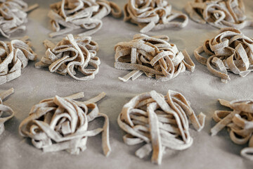 Homemade pasta. Dry fettuccine noodles in nests on baking tray close up. Making whole-grain pasta