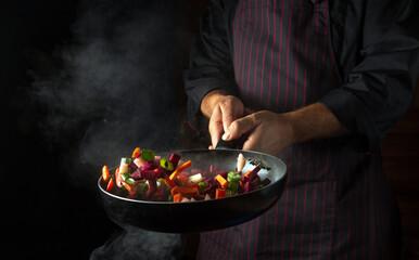Cooking vegetables on a hot frying pan in the hands of a chef. Molecular gastronomy or cuisine.