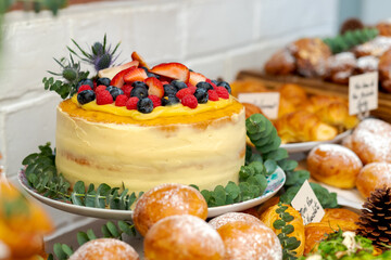 Vintage Fresh and delicious cake on a table with more snacks decorated in an elegant way. Berries cake decorated with eucalyptus leaves on a table surrounded by sweet preparations.