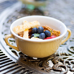 Little dessert bowl with greek yogurt and fruits on an ornamented iron table. Cup of meal on a table.