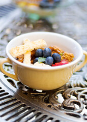 Little dessert bowl with greek yogurt and fruits on an ornamented iron table. Cup of meal on a table.