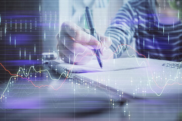 Financial forex graph drawn over hands taking notes background. Concept of research. Double exposure