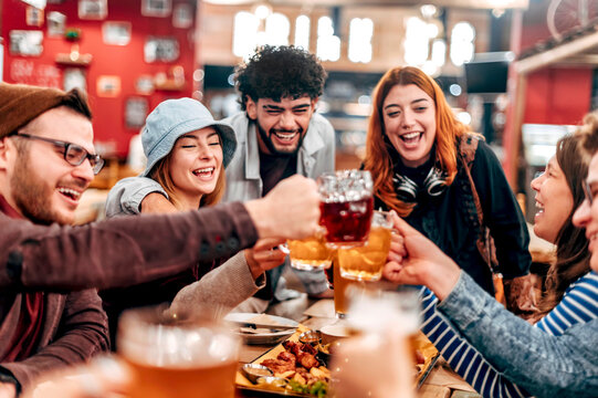 Group of happy friends drinking and toasting beer at brewery bar restaurant - Young people eating bbq at pub - Friendship concept with young people having fun together - Focus on chicken wing