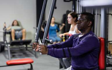 African american athlete works on special simulator for the development of pectoral muscles