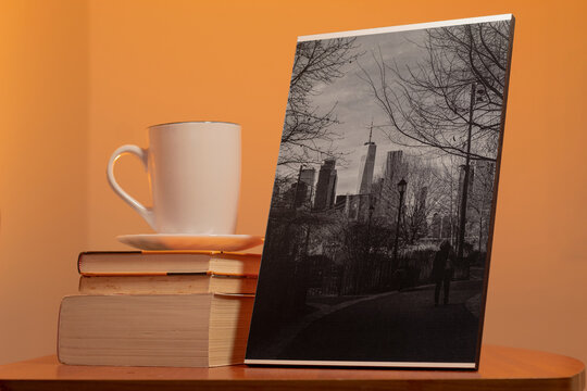 A photograph of New York next to three books and a cup of coffee on a nightstand inside a room