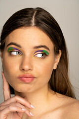 Pensive teenage model with colorful makeup looking away isolated on grey.